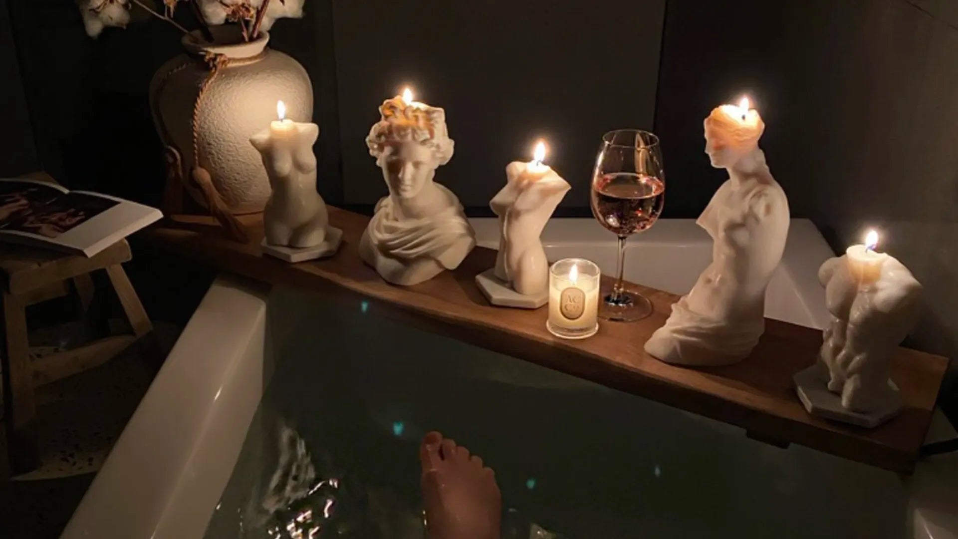 A wooden tray across the tub holds five statue-shaped candles with flickering flames, casting a serene candlelight for mental well-being.