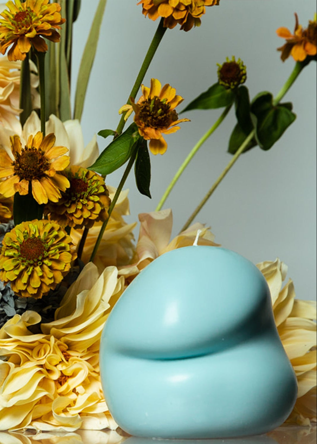 Blue tulum blobbie candle with yellow flowers on a light gray background