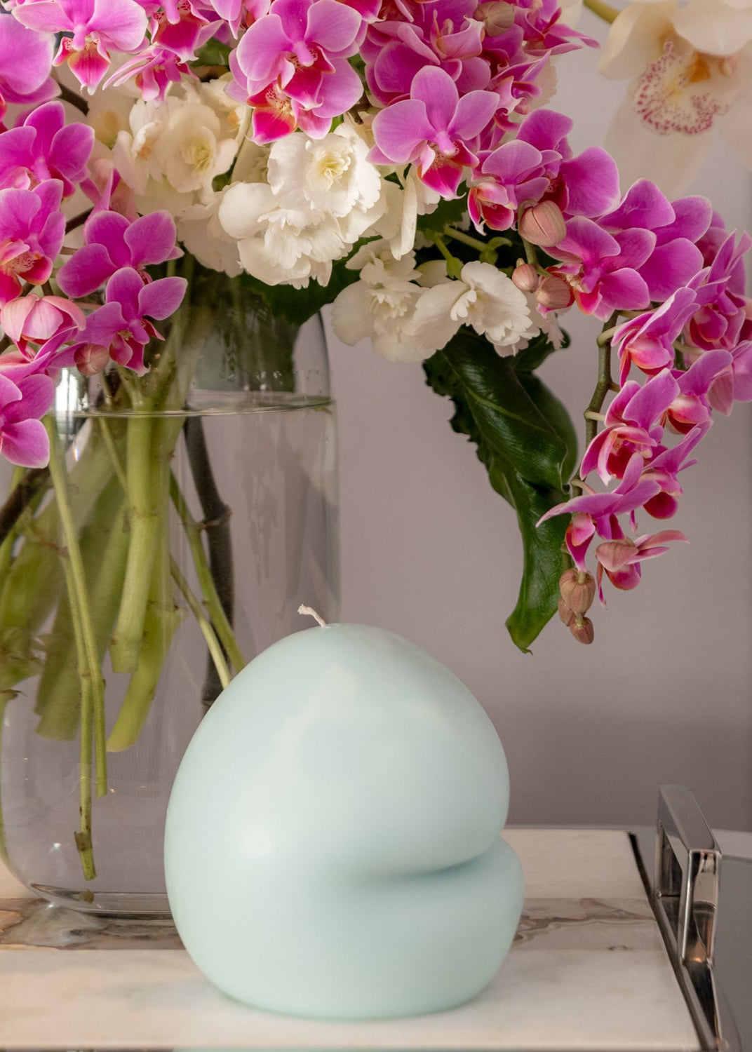 Glass vase with pink and white flowers on a surface with a light blue candle.