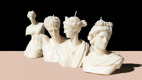 Four white candles, handcrafted by Ancient Candle Co, are shaped like classical statues depicting busts of ancient figures.