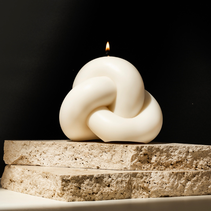 A beautifully designed sculptural candle in a knot shape, lit and displayed on stone blocks. This candle exemplifies the unique custom candles for wedding favours created by Ancient Candle Co.